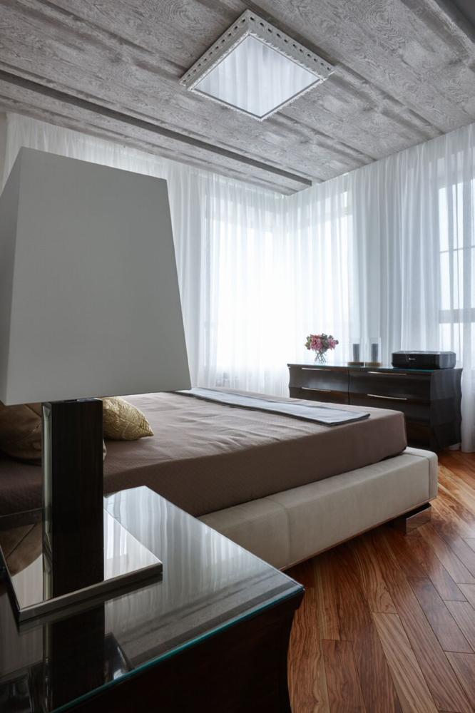 На потолке над кроватью проходят деревянные панели, плавно спускающиеся вниз по стене за изголовье кровати.